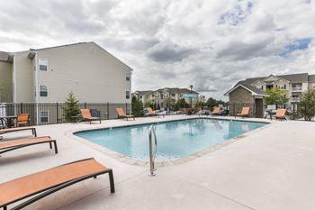 A pool with a slide and sun loungers in front of apartment buildings.